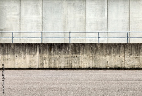 Railing on a grunge concrete wall dividing an asphalt road from a concrete building. Background for copy space.