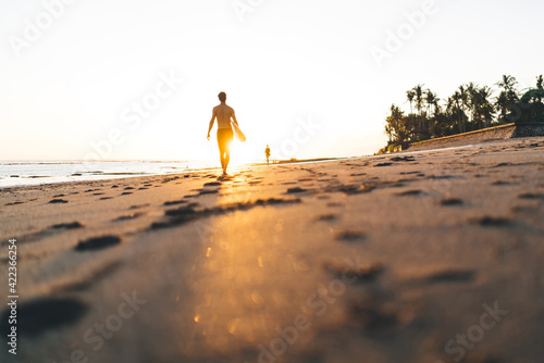 Faceless athlete strolling on beach with surfboard at bright sunset