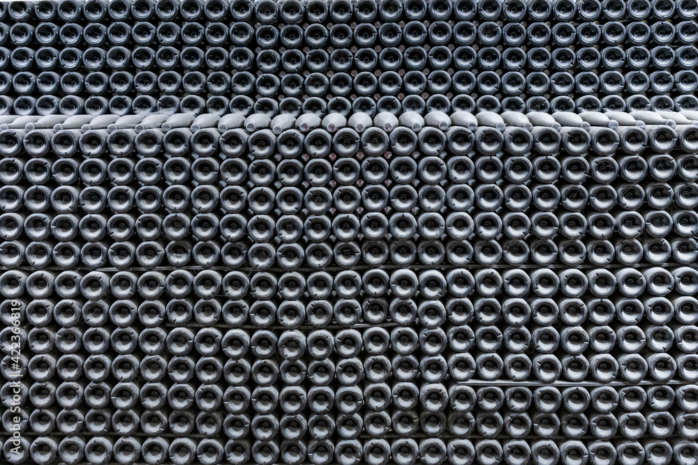 Wine cellar at the sparkling wine factory. Wine bottles, covered with a layer of grey dust, lie in long rows in many layers. Bottles bottoms create a geometric pattern Wine cellar at the sparkling wine factory. Wine bottles, covered with a layer of grey dust, lie in long rows in many layers. Bottles bottoms create a geometric pattern