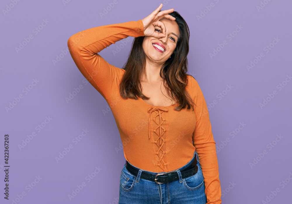 Beautiful hispanic woman wearing casual clothes smiling happy doing ok sign with hand on eye looking through fingers Beautiful hispanic woman wearing casual clothes smiling happy doing ok sign with hand on eye looking through fingers