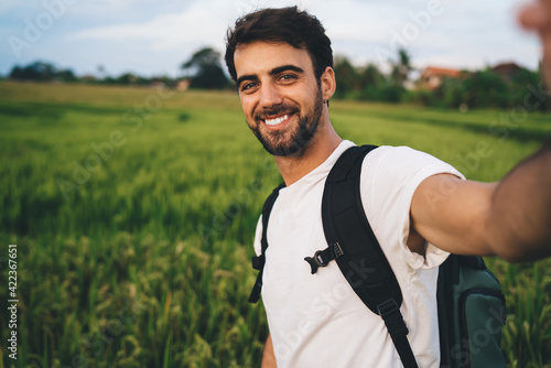 Smiling man holding camera and taking selfie on grassland