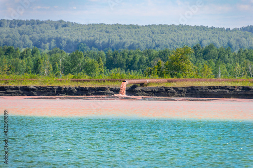 Konstfotografi a red-orange slurry pours out of a large rusty pipe, polluting the waters of a c