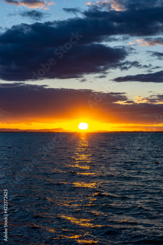 scenic and colorful sunset over the ocean with shimmering light on the waves and silhouette of mountains on the shore behind