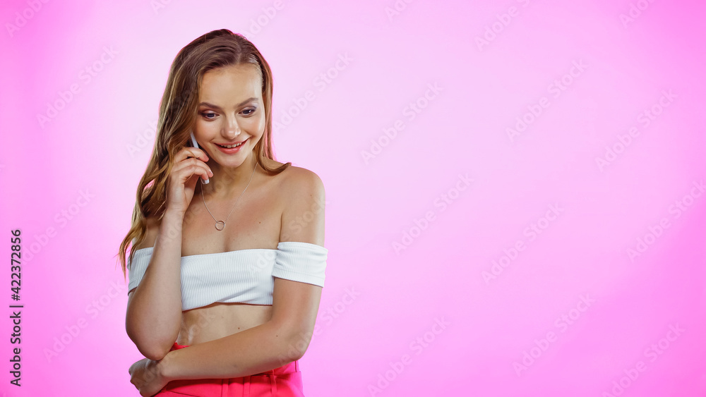 Young woman in crop top with naked shoulders talking on smartphone on pink Young woman in crop top with naked shoulders talking on smartphone on pink