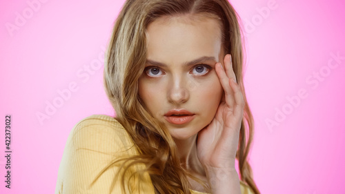 young woman with wavy hair looking at camera isolated on pink