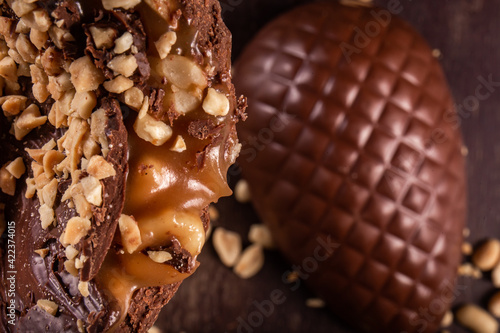 Photography Close up of a stuffed chocolate easter egg with peanut and caramel on a wooden table with lots of peanuts around