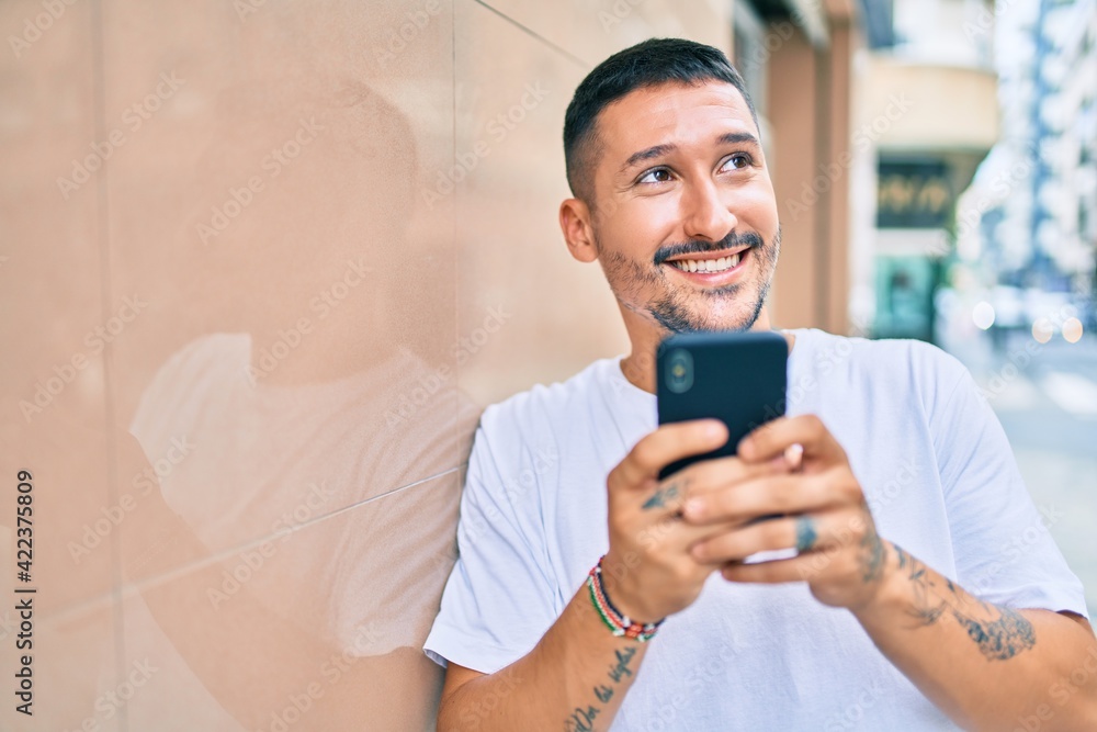 Young hispanic man smiling happy using smartphone leaning on the wall Young hispanic man smiling happy using smartphone leaning on the wall