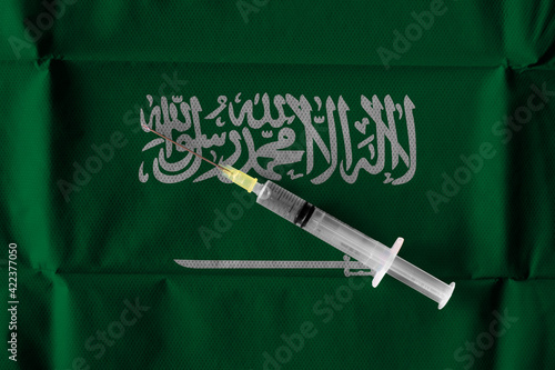 Concept of the ongoing efforts by Saudi Arabia to deliver and distribute COVID-19 Vaccine with a syringe ready to use on a Saudi flag.