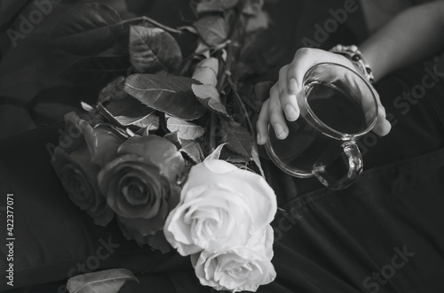 Close-up of a glass with tea in a female hand. A bouquet of roses, beautiful decoration. Black and white photography. photo