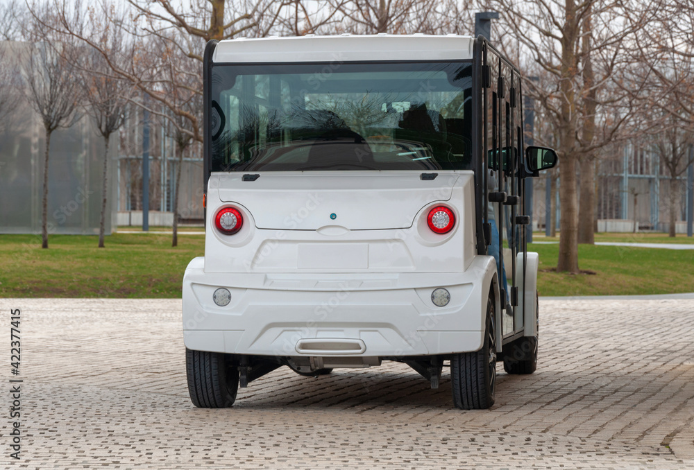 Electric street vehicle with zero emission stands near the wall in the park. The road is paved with cobblestones. Compact electric utility vehicle to transport guests to and from an event.