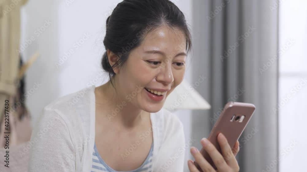 headshot asian happy pretty woman holding a phone is waving hi and talking happily during a video chat at home. headshot asian happy pretty woman holding a phone is waving hi and talking happily during a video chat at home.
