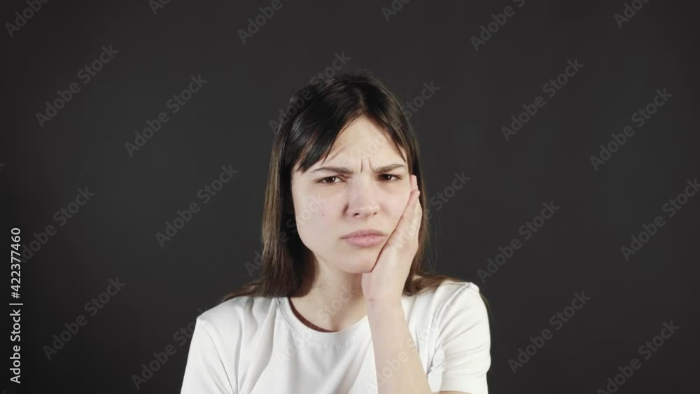 An unhappy young woman touches her cheek, suffers from a toothache, a ...