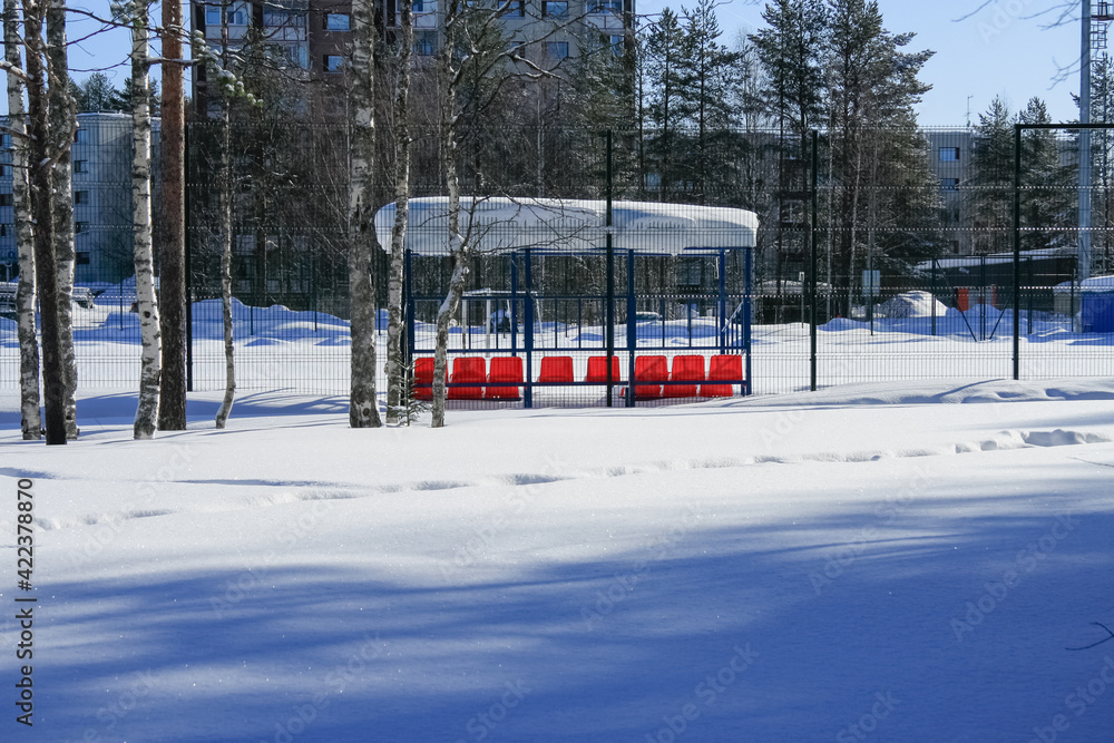 Naklejka premium Red chairs under a canopy in the snow on the football field.