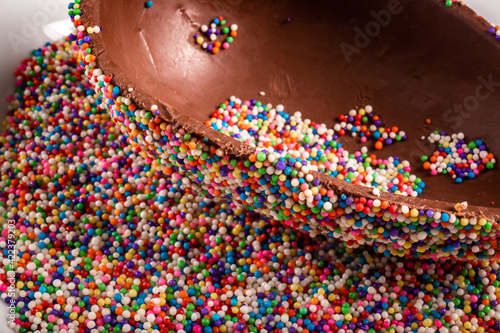 Close up of a colorful chocolate easter egg with sprinkles on a white plate.