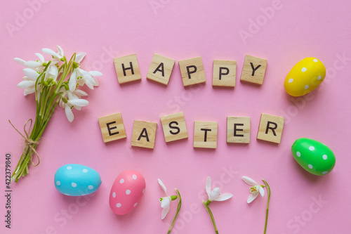 Delicate waterdrop flowers, colored eggs and the inscription Happy Easter on light pink background with copy space. Flat lay, top view