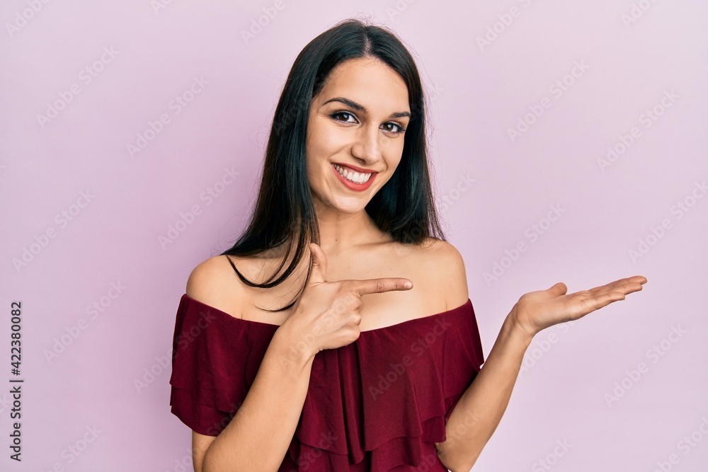 Obraz premium Young hispanic woman wearing casual clothes amazed and smiling to the camera while presenting with hand and pointing with finger.