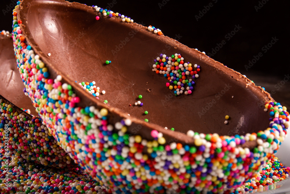 Close up of a colorful chocolate easter egg with sprinkles on a white plate.