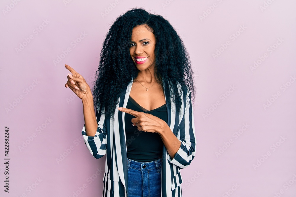 Middle age african american woman wearing casual clothes smiling and looking at the camera pointing with two hands and fingers to the side.