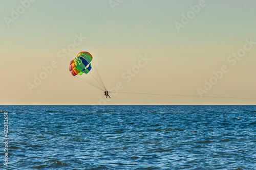 Man and woman tourists are flying on parasailing over the sea against the backdrop of the sunset sky and the horizon. Extreme vacation concept