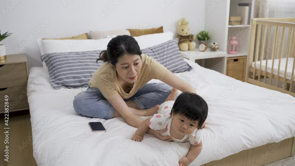 asian mother is picking her curious young child up from the edge of bed to prevent falling while playing with her in the bedroom at home. asian mother is picking her curious young child up from the edge of bed to prevent falling while playing with her in the bedroom at home.