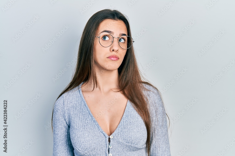 Young brunette teenager wearing casual sweater and glasses smiling looking to the side and staring away thinking. Young brunette teenager wearing casual sweater and glasses smiling looking to the side and staring away thinking.
