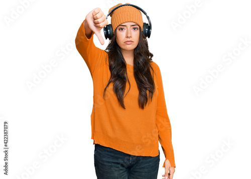 Beautiful brunette young woman listening to music using headphones looking unhappy and angry showing rejection and negative with thumbs down gesture. bad expression. © Krakenimages.com