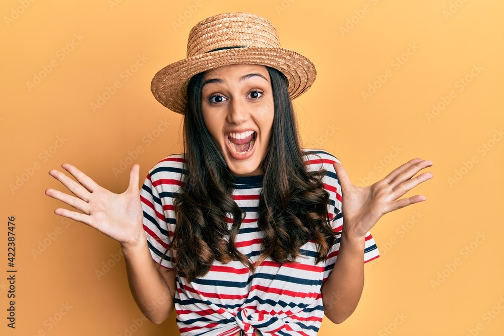 Young hispanic woman wearing summer hat celebrating victory with happy smile and winner expression with raised hands Young hispanic woman wearing summer hat celebrating victory with happy smile and winner expression with raised hands