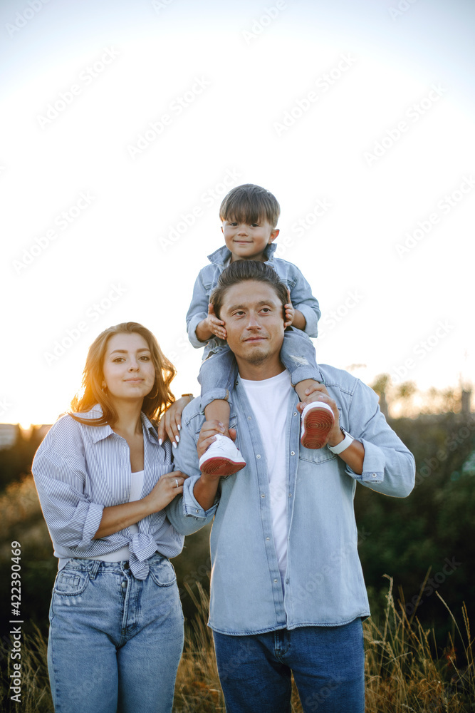 happy young family outdoors. the boy sits on dad's shoulders. cheerful joyful family outdoors at sunset. stylish family in casual clothes.