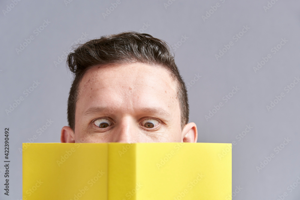 Young man reading a yellow book with squinted eyes; a comical, funny look Young man reading a yellow book with squinted eyes; a comical, funny look