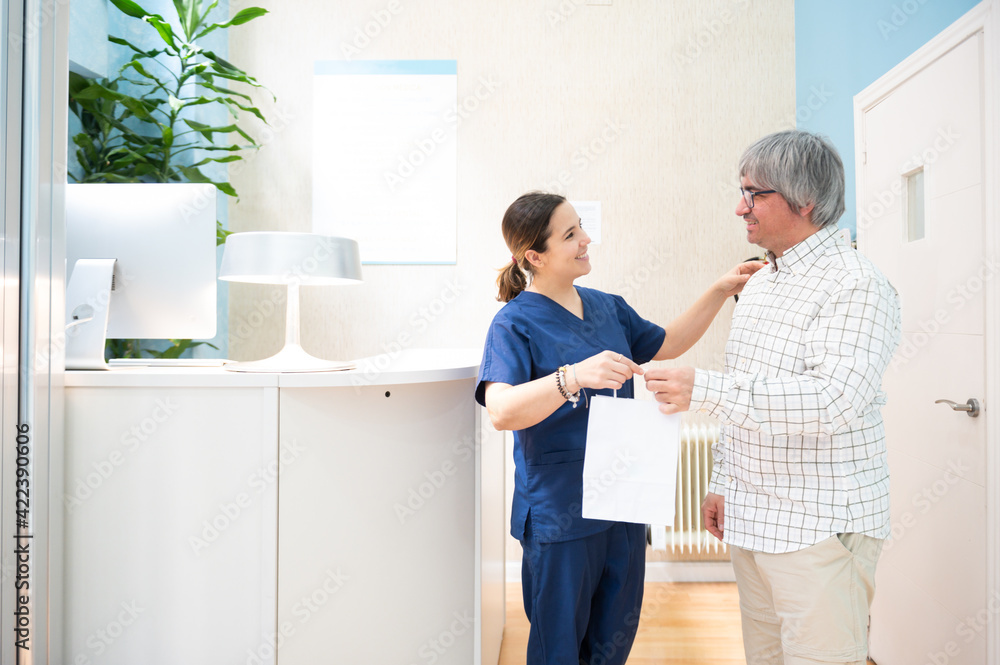 Fototapeta premium Attractive young doctor bidding farewell to her happy patient with a bag of products courtesy of the dental clinic.
