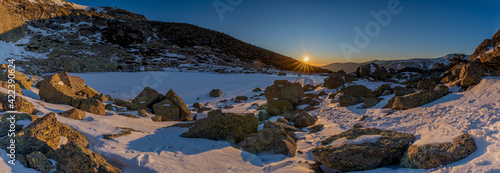 panoramic view of the sunrise or sunset of the sun over the mountains with a snow lake  © Gustavo Palacios