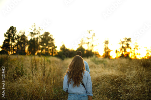 woman with wavy hair follows the man in the field at sunset. girl walks in the park outdoors. beautiful sunset rays in the forest 