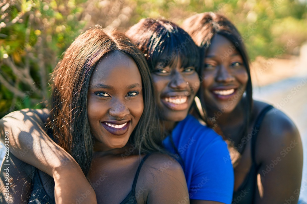 Fototapeta premium Three african american friends smiling happy sitting on the bench at the park.
