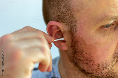 Photo of a young man cleaning ears with cotton sticks at home. Cropped shot of young male hand holding ear stick. Close up of a male about to use a cotton swab in his ear. Selective focus.