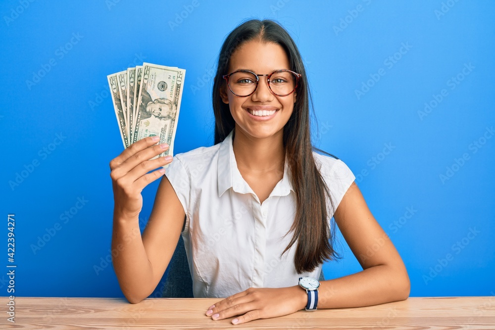 Beautiful hispanic woman holding 20 dollars banknotes looking positive and happy standing and smiling with a confident smile showing teeth Beautiful hispanic woman holding 20 dollars banknotes looking positive and happy standing and smiling with a confident smile showing teeth