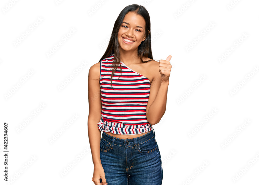 Beautiful hispanic woman wearing casual clothes smiling with happy face looking and pointing to the side with thumb up. Beautiful hispanic woman wearing casual clothes smiling with happy face looking and pointing to the side with thumb up.