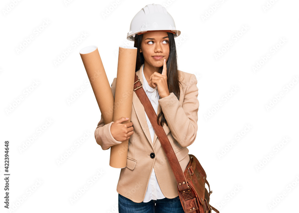 Beautiful hispanic woman holding paper blueprints serious face thinking about question with hand on chin, thoughtful about confusing idea Beautiful hispanic woman holding paper blueprints serious face thinking about question with hand on chin, thoughtful about confusing idea
