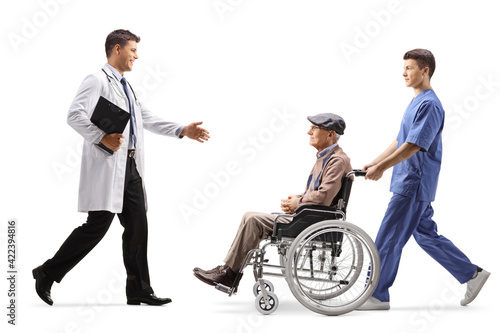 Full length profile shot of a male doctor greeting elderly patient in a wheelchair