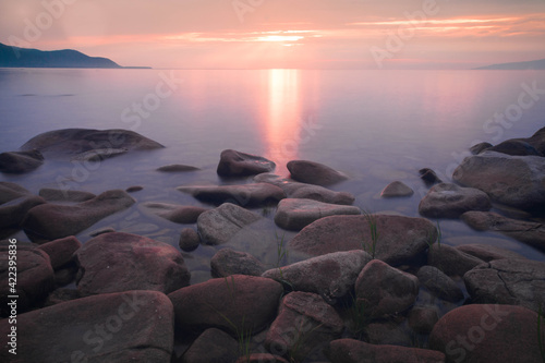 Many stones in a semicircle and mountains in the distance under a pink sunset and purple water on Baikal