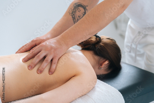 Close-up view of male masseur massaging back and shoulder blades of female lying on massage table at spa salon. Beautiful young woman with perfect skin getting relaxing massage.