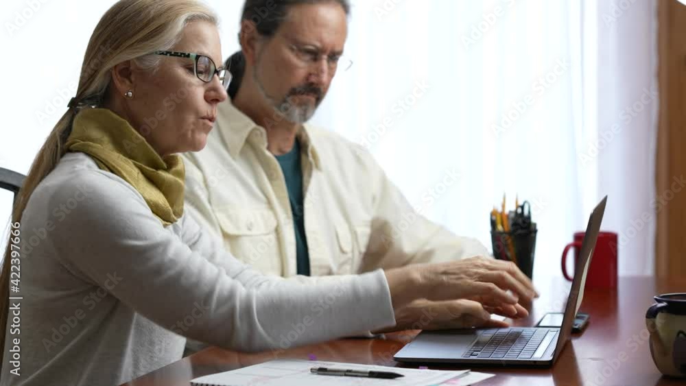 Mature couple at home working on laptop computer. Concept of man and woman remote working together. Mature couple at home working on laptop computer. Concept of man and woman remote working together.
