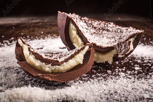 Cracked chocolate easter egg with coconut filling and grated coconut on the top on a wooden table.