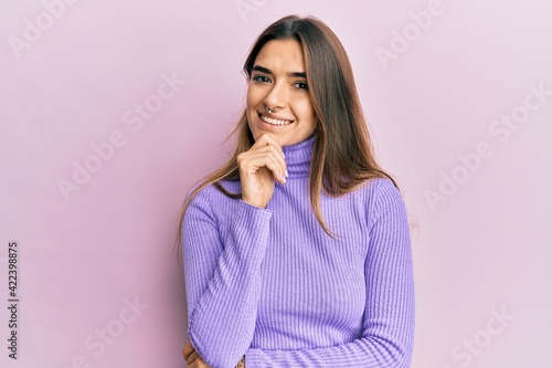 Young hispanic woman wearing casual clothes smiling looking confident at the camera with crossed arms and hand on chin. thinking positive.