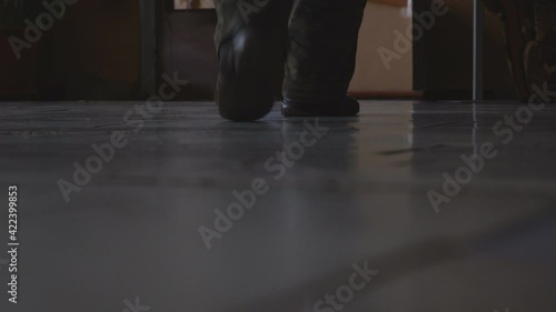 The feet of a man in sneakers walking away from the camera in a dark room. The legs move away from the camera. Low angle view. Low key