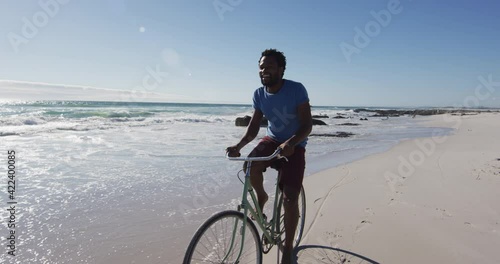 African american man smiling and riding bike on the beach