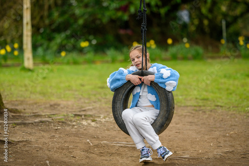 Girl on a Tyre Swing. A young girl waving and smiling while swinging on a black tyre swing at a park.