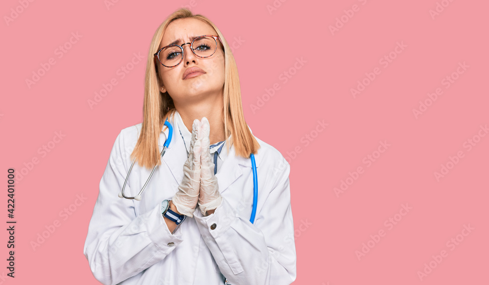 Beautiful caucasian woman wearing doctor uniform and stethoscope begging and praying with hands together with hope expression on face very emotional and worried. begging. Beautiful caucasian woman wearing doctor uniform and stethoscope begging and praying with hands together with hope expression on face very emotional and worried. begging.