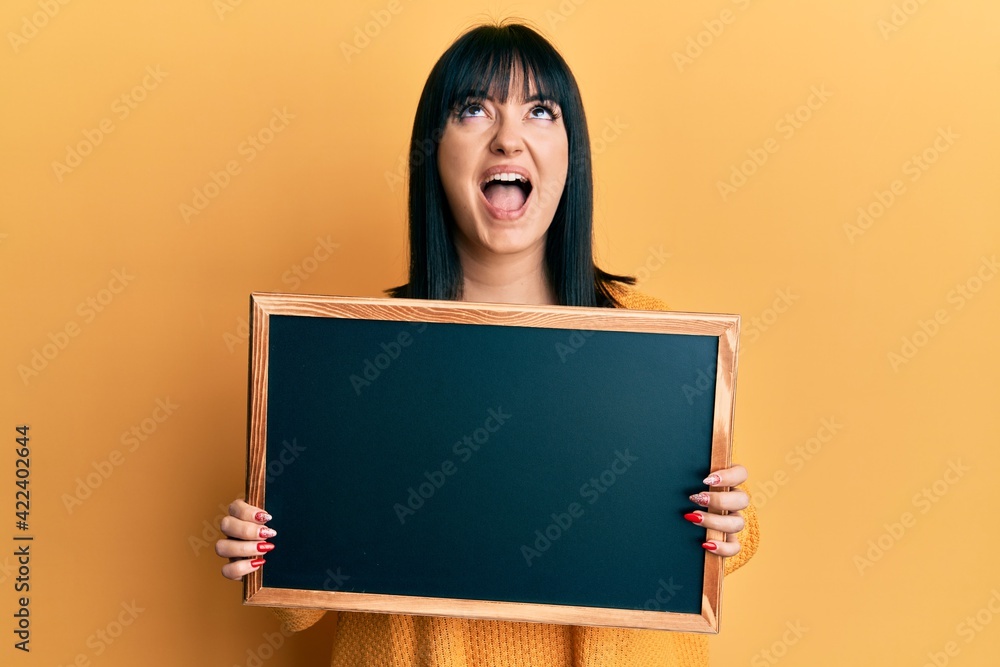 Young hispanic woman holding blackboard angry and mad screaming frustrated and furious, shouting with anger looking up. Young hispanic woman holding blackboard angry and mad screaming frustrated and furious, shouting with anger looking up.