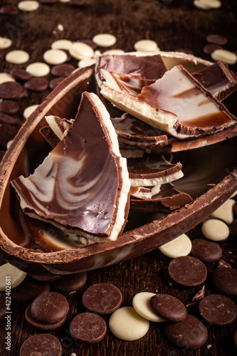 Wall Mural Dark and white chocolate easter egg with cracked eggs inside and lots of chocolate chips all around on a wooden table
