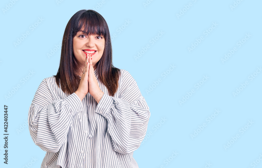 Young plus size woman wearing casual clothes praying with hands together asking for forgiveness smiling confident. Young plus size woman wearing casual clothes praying with hands together asking for forgiveness smiling confident.